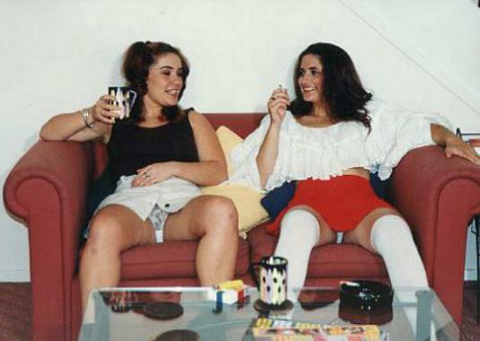 two women chatting on a couch, one smoking, showing their knickers